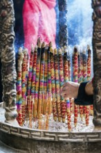 Cropped unrecognizable person holding a vibrant, large incense sticks burning, with smoke rising in