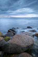 Rocks in the foreground lead to a bridge running across the sea in the distance, Öresund Bridge,
