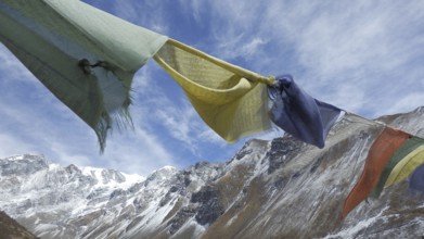 Colourful prayer flags flying in close-up against a background of a snowy mountain range, hiking in