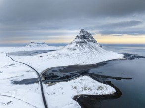 A breathtaking aerial view of Kirkjufell mountain in Iceland, covered in snow, surrounded by icy