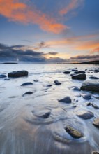 Orange coloured cloudy sky at sunset on a sandy beach strewn with round stones near Achiltibuie on