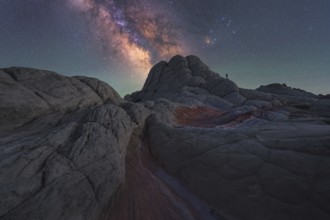A lone man stands under the majestic Milky Way galaxy in the surreal, alien-like landscape of White