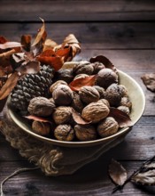 A cozy autumn still life featuring a bowl of walnuts, pine cone, and dried leaves on a rustic