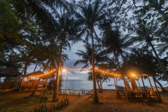 A serene beach view in the Philippines with bamboo huts lit by warm lights at twilight, showcasing