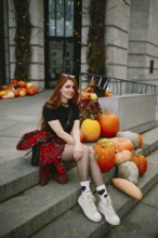 A young woman in autumnal attire sits on stone steps adorned with pumpkins in an urban Montreal