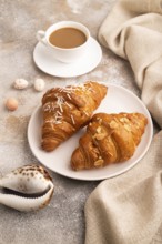 Croissant on white plate on brown concrete background and linen textile, cup of coffee, side view,