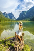 Young woman wearing a straw hat sitting on a tree stump by lake dobbiaco, enjoying the breathtaking
