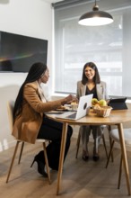Two businesswomen are enjoying breakfast and working together in a hotel room during a business