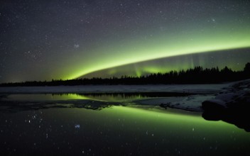 Aurora borealis in green colors over lake in snow covered landscape at night, Lapland, Finland