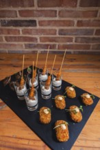 Elegant black slate platter featuring gourmet skewered appetizers in shot glasses with creamy