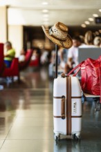 White suitcase adorned with a cowboy hat, indicating travel and adventure, located in a busy