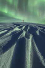 Unrecognizable person stands alone under the mesmerizing Aurora Borealis on a snowy landscape