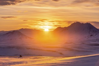 A stunning winter sunset illuminates Iceland's snowy mountains, casting a warm glow across vast,