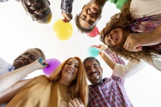 A cheerful group of friends looks down at the camera, holding colorful balloons, symbolizing a