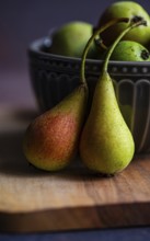 Close up of two wild pears resting on a wooden board with a decorative ceramic bowl filled with