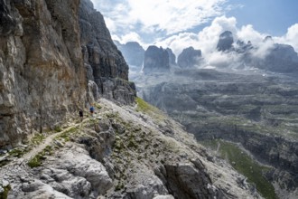Two mountaineers on a hiking trail in front of a picturesque mountain landscape with rocky peaks,