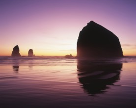 A serene sunset graces the horizon, illuminating ocean waters and silhouetting majestic rock
