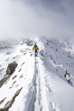 Mountaineer climbing up the narrow ridge of Piz Laviner, view of wintry mountain landscape, Grisons
