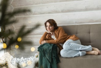 A woman sits cozily on a couch, adorned in a warm orange sweater and light blue jeans, gently
