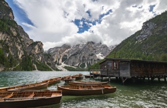 Traditional wooden rowboats rest near a rustic wooden boathouse on Lago di Braies, surrounded by