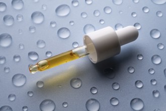 A close-up of a pipette bottle containing vitamin C serum, placed on a surface with scattered water