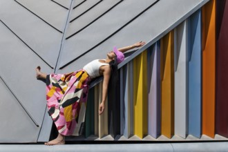 A woman in a vibrant, colorful outfit contrasts strikingly with modern architectural design,