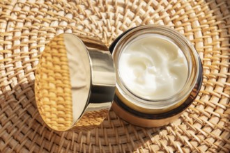 A luxurious skincare cream cosmetic with a golden lid rests on a woven mat. The rich cream inside