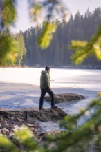 Man looking at a frozen lake, surrounded by coniferous forests and sunlight, Glaswaldsee, Bad