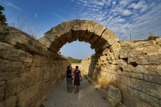 Crypt, vaulted passage to the stadium, two people walking through an ancient stone arch pass under