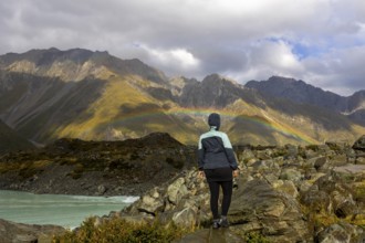 A woman stands on rocky terrain, admiring a vibrant autumn landscape on Mount Cook, New Zealand,