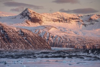 A breathtaking winter sunrise casts a warm glow over the snow-capped mountains and icy landscape in