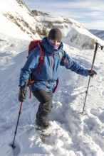 Adventurer in blue jacket and red backpack enjoys ski touring on a sunny day. Using poles for