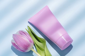 Top view of a vibrant pink cosmetic tube alongside a delicate pink tulip, perfectly arranged on a
