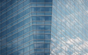 Close-up of a modern glass building facade reflecting a clear blue sky and fluffy clouds,