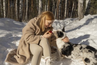 A woman and her Border Collie dog share a moment in a snowy forest. The woman, visible in full,