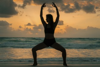 Silhouette of a woman practicing yoga on a beach during sunrise in Tulum, Mexico. The serene