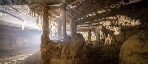 A deep underground excavation reveals exposed soil columns and eroded concrete structures. The dim