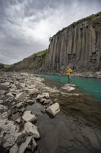 Tourist standing by the river in Stuðlagil Canyon, turquoise blue river between basalt columns,