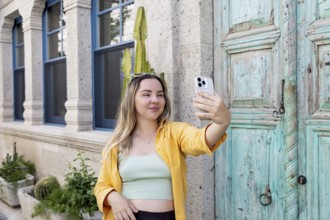A woman takes a selfie on a charming street, wearing sunglasses and a yellow shirt. She stands in