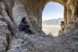 A climber rests on rocky terrain while two others practice mountaineering and rappelling in