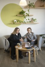Two women engage in a business meeting at a cozy cafe. They are discussing something on a tablet,