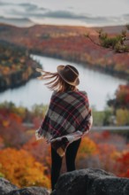 A woman in a hat and plaid shawl stands overlooking a picturesque Quebec landscape in autumn. The
