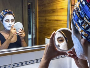 A woman examines her skincare routine using a hand mirror in a cozy bathroom of Victoria, Australia
