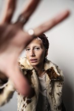 A woman wearing a stylish fur coat poses with hands stretched toward the camera. They sport bold