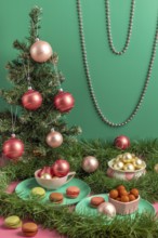Small Christmas tree with baubles and macaroons in pink and green, surrounded by decorations