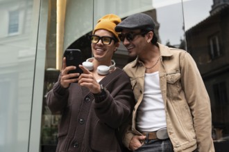 A joyful gay couple shares a moment of laughter while looking at a smartphone. They stand together