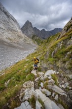 A mountaineer on a hiking trail with lush green vegetation, hiking trail to the Wolayerseehütte,