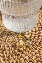 Close-up view of Omega 3 fish oil and vitamin D3 capsules on a woven rattan tray alongside a glass