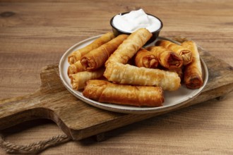 Fried spring rolls with cheese, on a wooden background, with cream sauce, no people