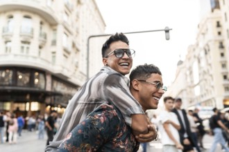 A cheerful latin gay couple enjoying a playful piggyback ride on a lively street in Madrid,